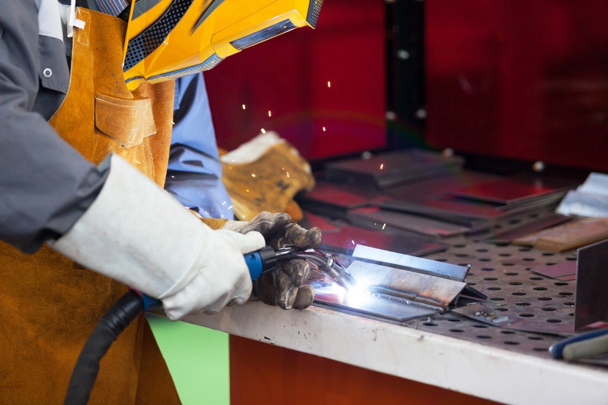 Welder performing TIG with torch in one hand, filler rod in the other, and a foot pedal for amperage control
