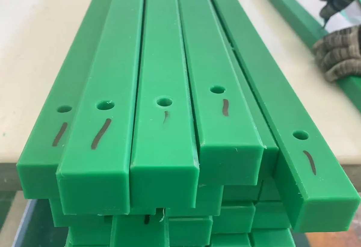 Cut and machined green UHMW polyethylene bars with drilled mounting holes for guide or wear components