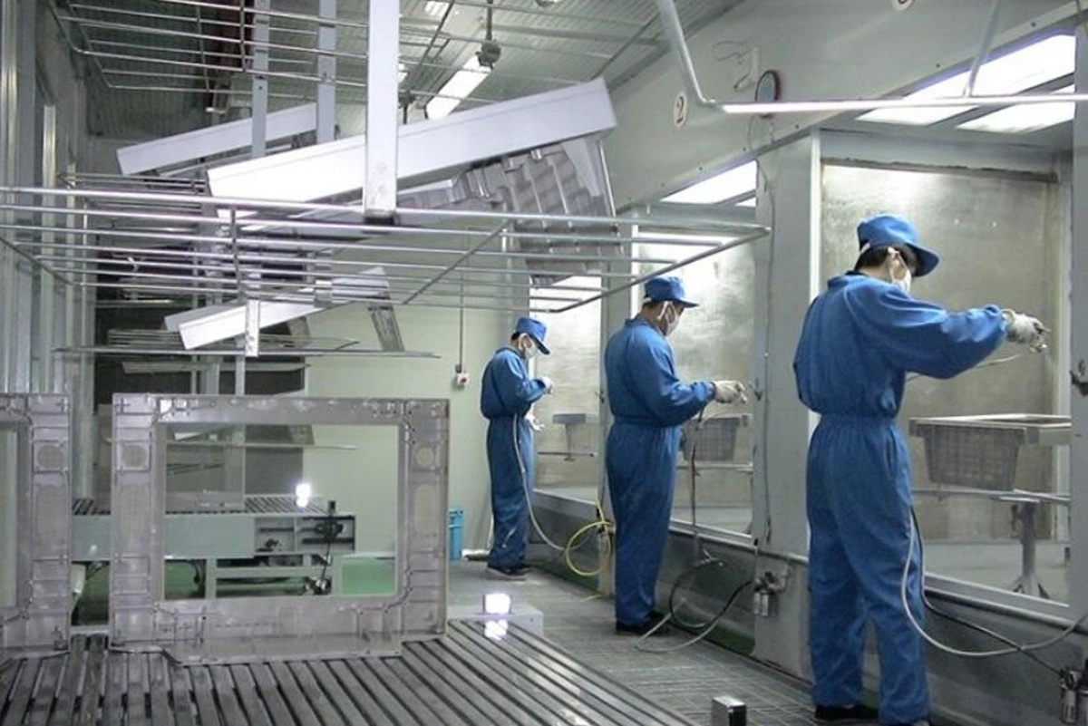 Workers applying powder coating in spray booth